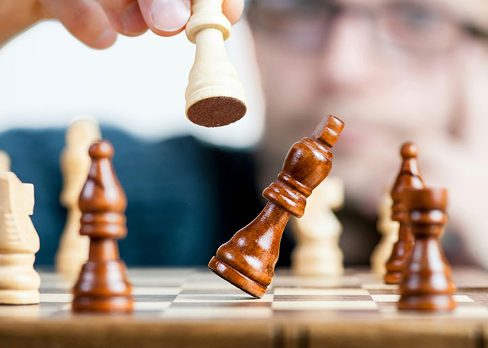 Person playing chess, hand moving pieces strategically, illustrating life cheat codes concept.