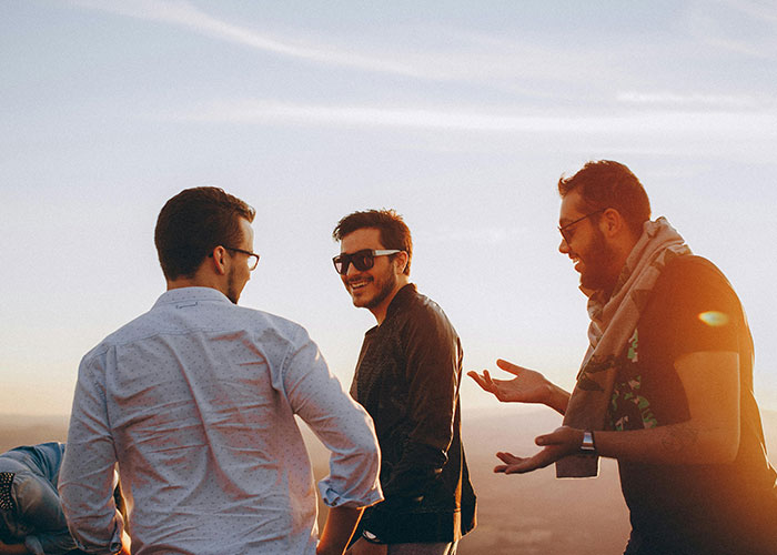 Three friends sharing life cheat codes outdoors, wearing sunglasses, enjoying a sunny day.