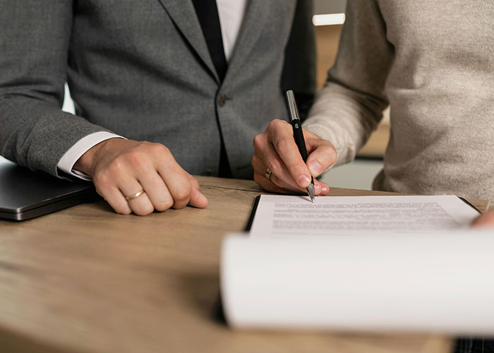 Two people in a meeting, one pointing with a pen at a document, discussing life cheat codes.