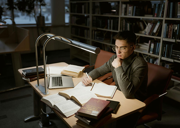 Person studying with books and laptop at a library desk, exploring life cheat codes for effective learning strategies.