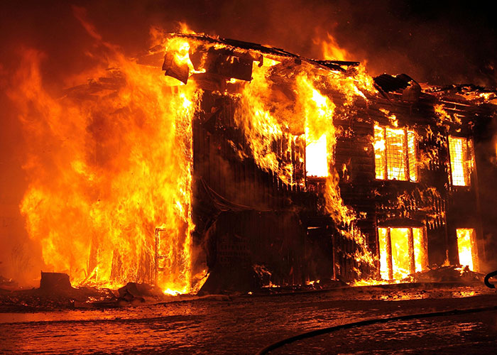 Burning house engulfed in flames during the night, illustrating life challenges and unexpected events.