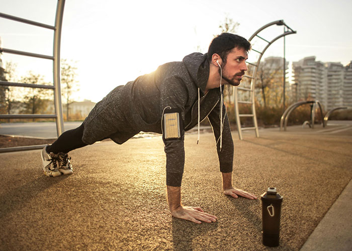 Man doing push-ups outdoors, listening to music, illustrating life cheat codes for effective workouts.