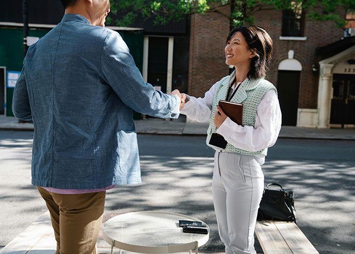 Two people shaking hands on a street, exchanging life cheat codes, one holding a tablet.