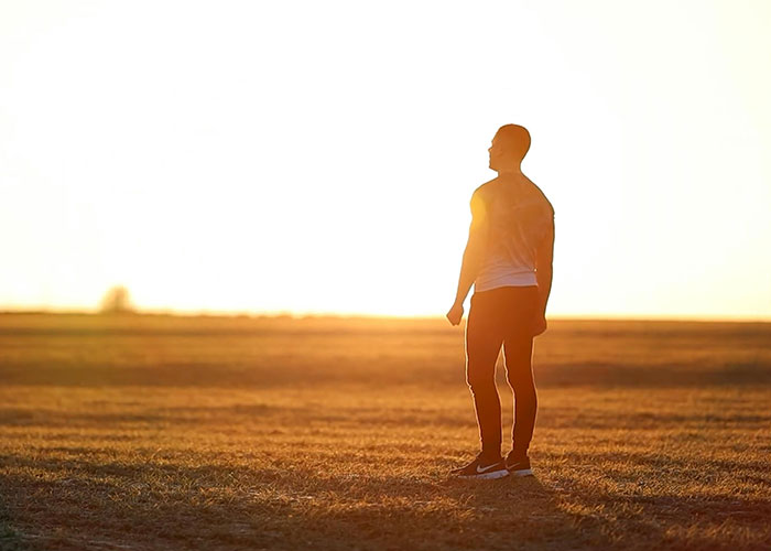 Person standing in a field during sunset, capturing a serene moment in life.