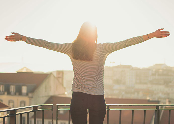 Person embracing the sunrise on a balcony, representing life's cheat codes in a serene setting.