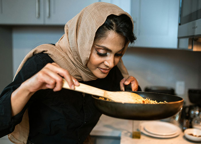 Woman cooking with a wooden spatula and enjoying the aroma, using life cheat codes in the kitchen.