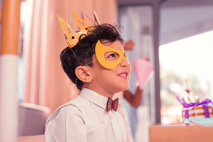 Young boy wearing a crown and mask with a child-party-bag in the background.