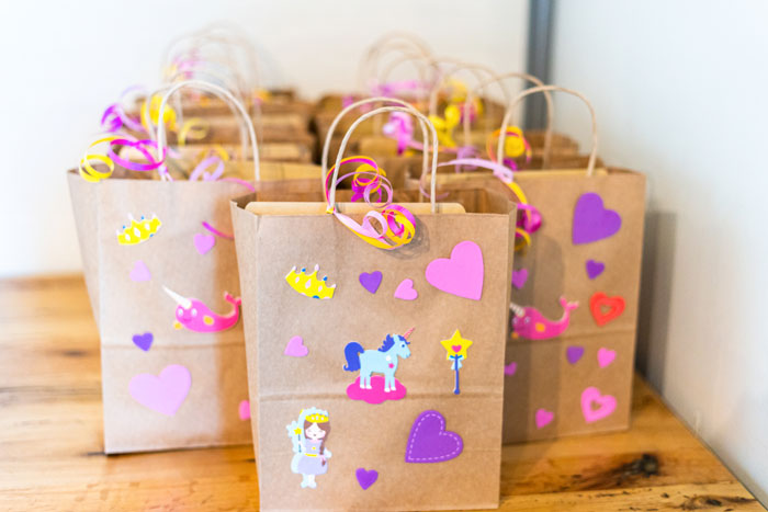 Child-party-bag decorated with colorful stickers and filled with goodies, placed on a wooden table.