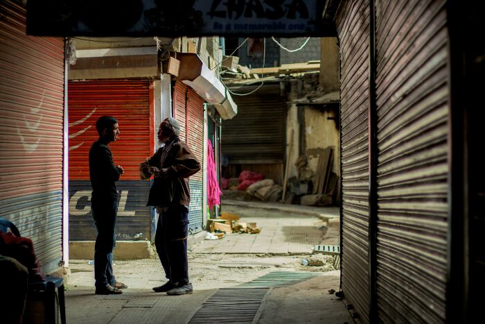 Two people conversing in a narrow alley with closed shop shutters, showcasing human genius in an urban setting.