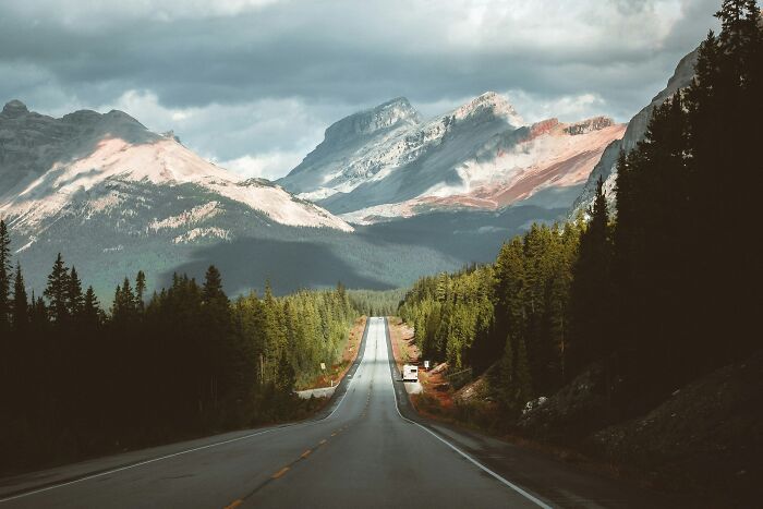 Scenic road through a forest leading to majestic mountains under dramatic skies in the Tuscany region of Italy.