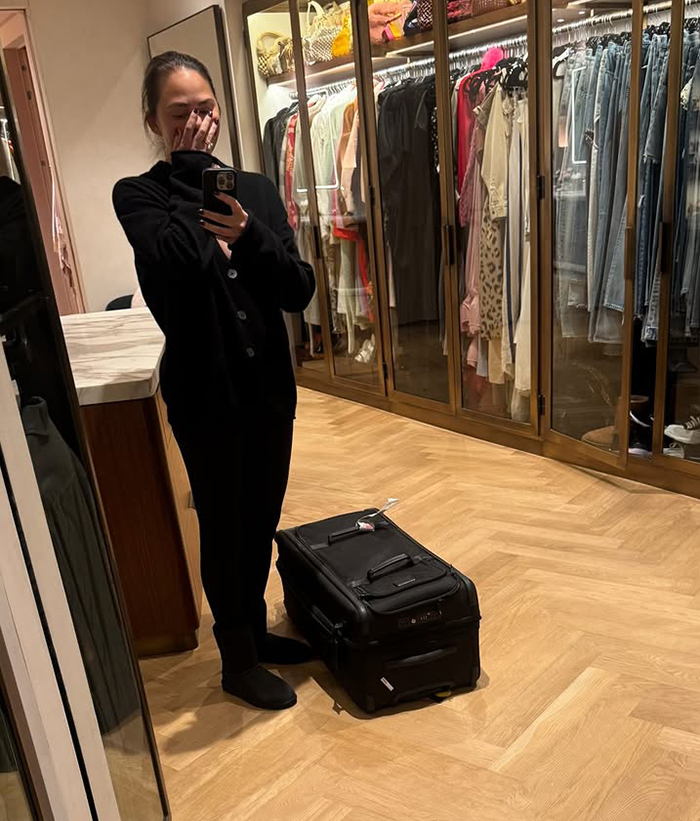 Celebrity in a closet, holding a phone with a suitcase nearby, amidst criticism during LA wildfires.