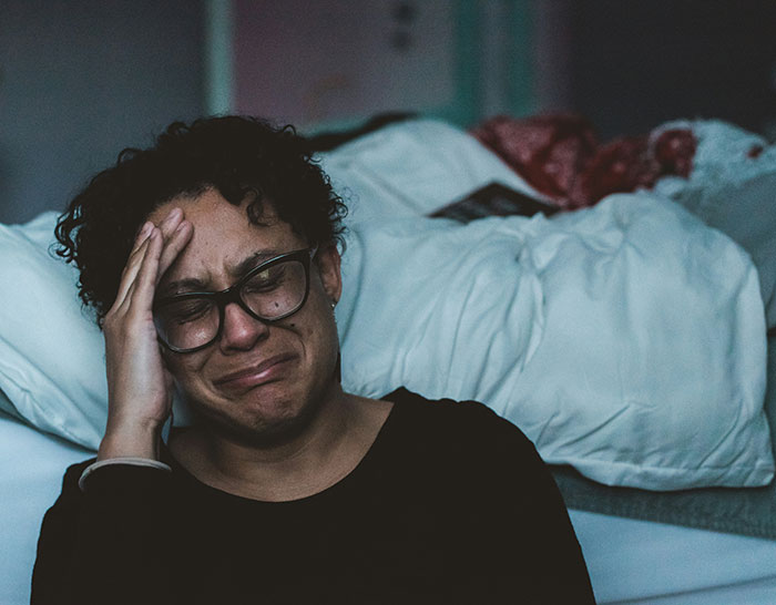 Crying woman sitting by the bed, hand on head, reflecting a theme of betrayal and homelessness.