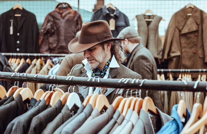 Man in a hat browsing through jackets at a store.