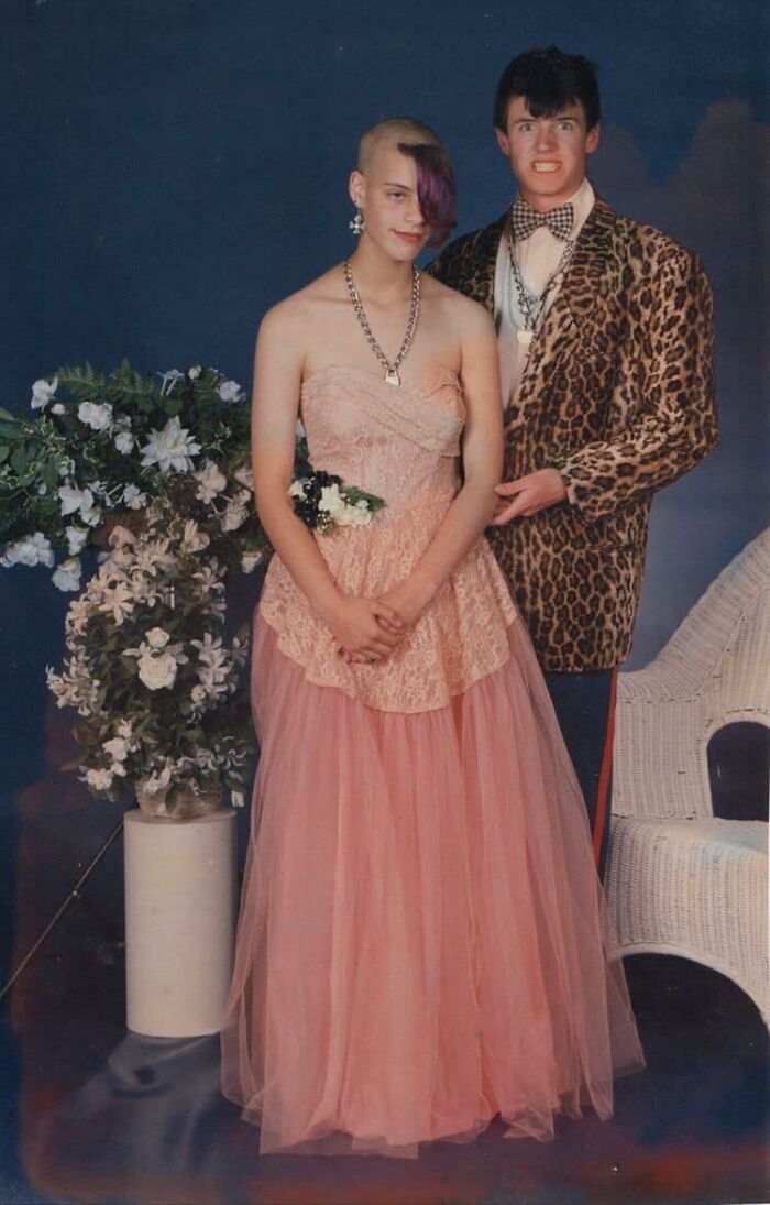 Teen in a formal dress with a unique hairstyle poses next to a friend in a leopard print jacket, highlighting a hair accident.