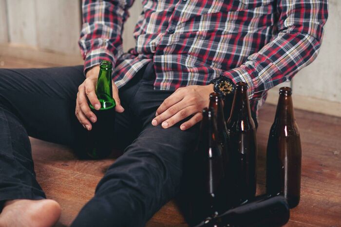 Person in a plaid shirt sitting on the floor with beer bottles, reflecting on things not realized as messed up until older.