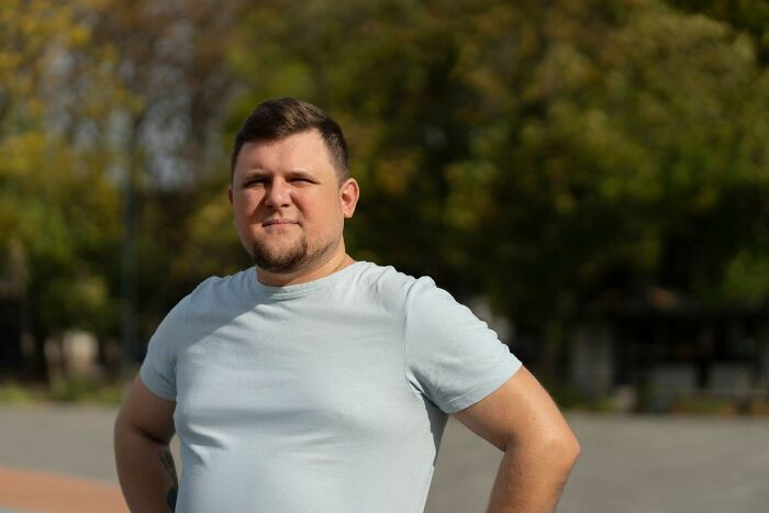 Man standing outdoors on a sunny day, wearing a light blue t-shirt.