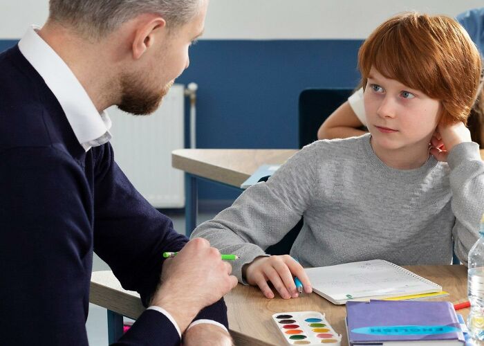 A child listening to an adult in a classroom, illustrating something you didn’t realize was messed up until older.