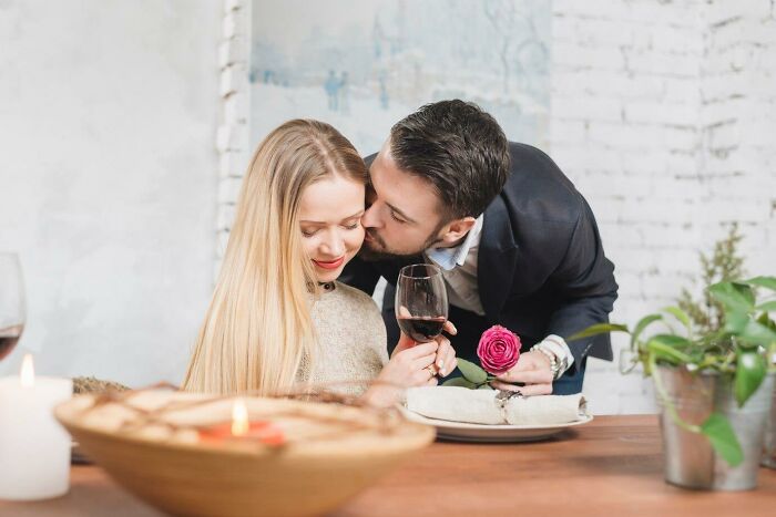 Couple embracing at a romantic dinner, man holding a rose and whispering to woman, reflecting on what’s messed up when older.