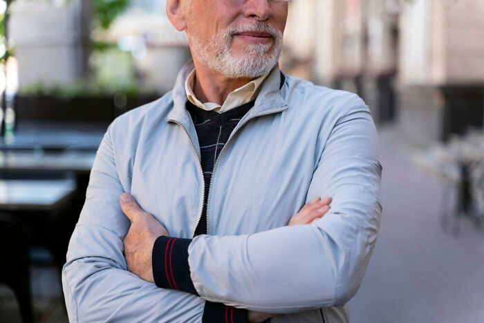 Elderly man in a city street, wearing a light jacket, reflecting on things he realized were messed up later in life.