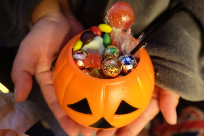 Hands holding pumpkin container filled with candy, illustrating millennials engaging in playful adulthood activities.