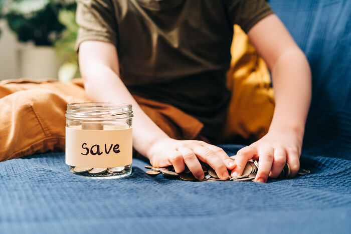 Child counting coins next to a jar labeled "Save," symbolizing challenges for the middle class with increasing unaffordability.