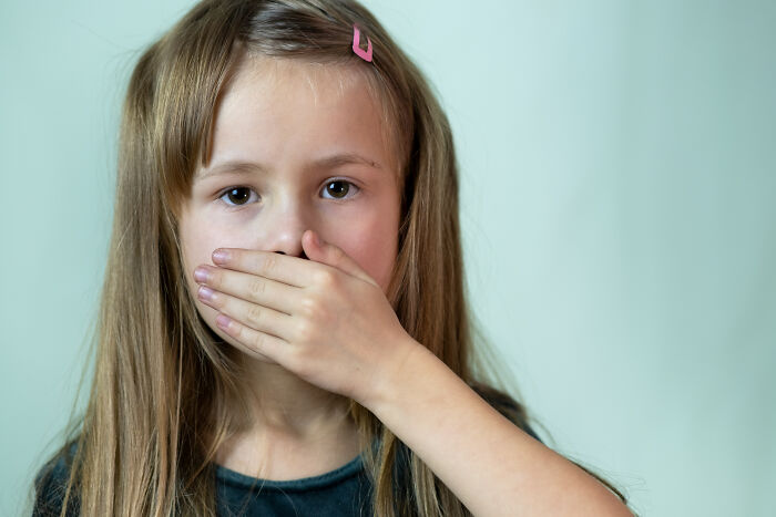 Young girl covering her mouth, highlighting the impact of horrible parenting behaviors.