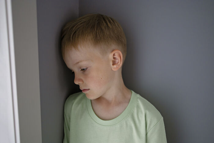 A sad child in a green shirt leans against a wall, reflecting the impact of horrible parenting.