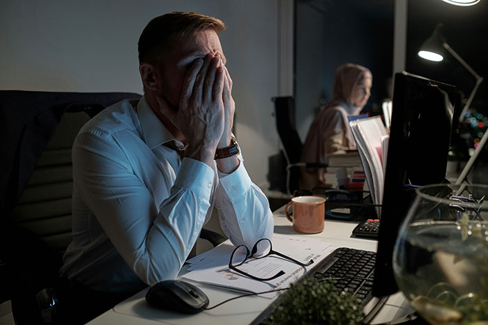 Man at desk, stressed, hands on face; software team chaos concept.