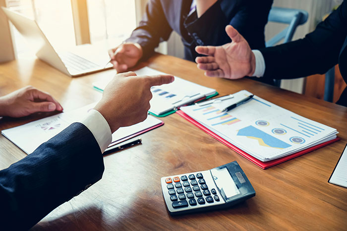 Business meeting with management discussing software processes, showing reports and a calculator on the table.