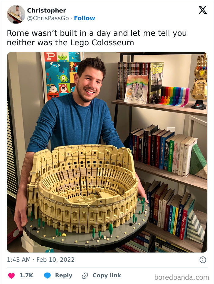 Man proudly holding a detailed LEGO Colosseum model, showcasing a cool LEGO build on a bookshelf background.