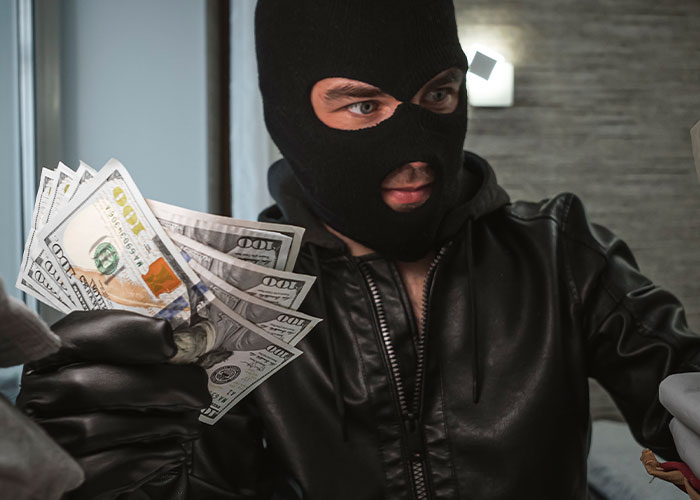 A masked individual in black leather holding a stack of cash, symbolizing dark family secrets.