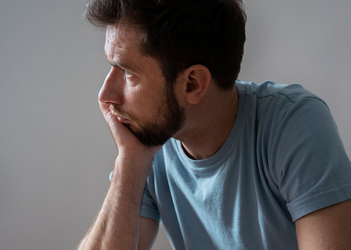 A pensive man in a blue shirt pondering over dark family secrets.