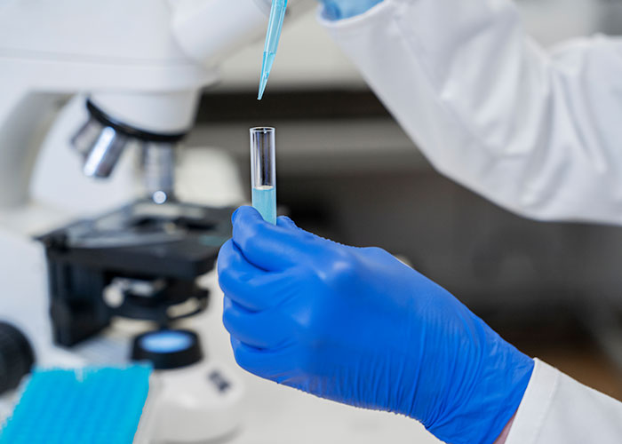 Scientist with blue gloves handling test tube near microscope in lab, reflecting secrets of scientific research.