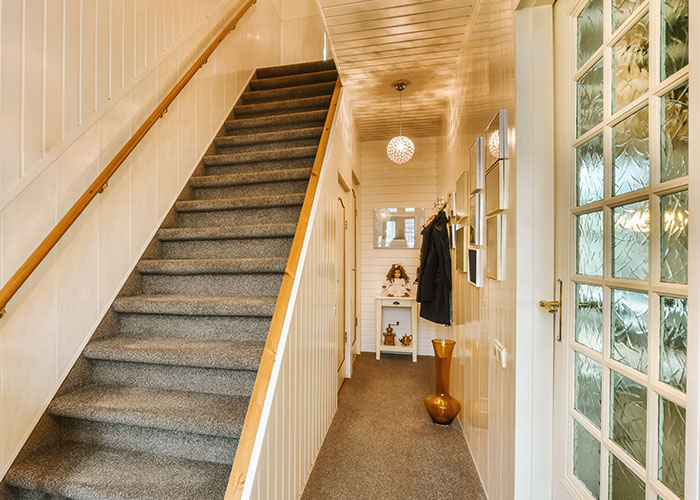 Hallway with carpeted stairs, warm lighting, and decor. Secrets theme suggested by mysterious ambiance.