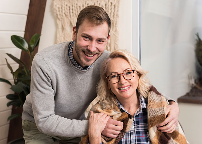 "Smiling man and woman, wrapped in a blanket, sitting in a cozy room, representing warm family moments."