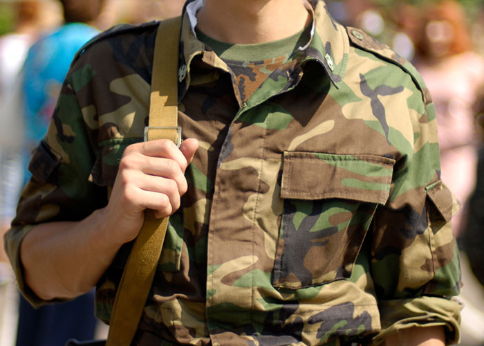 Person in camouflage holding a strap, symbolizing hidden family secrets.