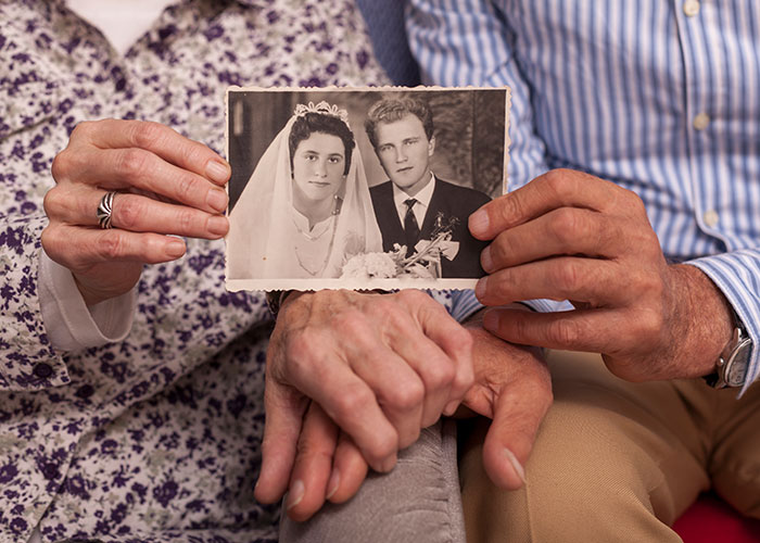 Elderly couple holding a vintage wedding photo, symbolizing untold family secrets.