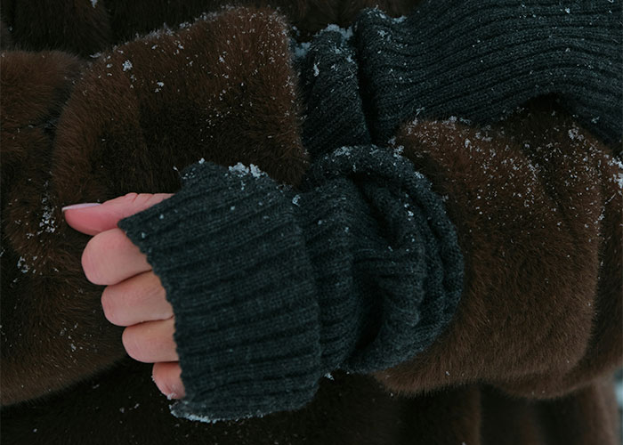 Close-up of hands in a brown fur coat and dark gloves, covered in snowflakes, reflecting unsettling medical conditions.