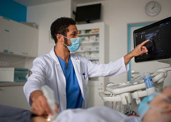 Medical professional examines ultrasound monitor in hospital setting.