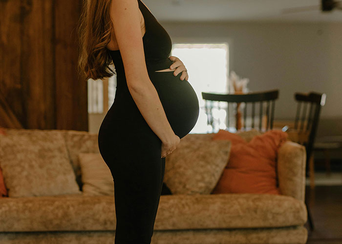 Pregnant woman standing sideways, holding belly in a cozy living room, illustrating medical concepts.