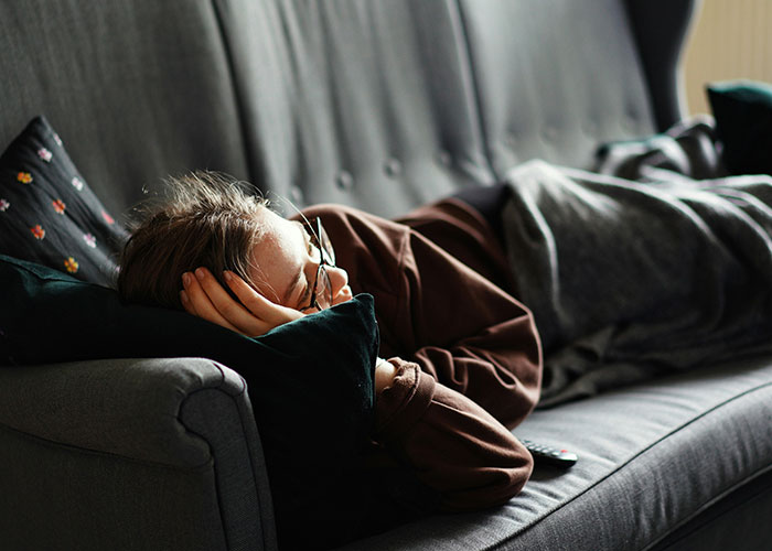 Person lying on a couch, wrapped in a blanket, appearing tired or unwell, possibly related to unsettling medical facts.