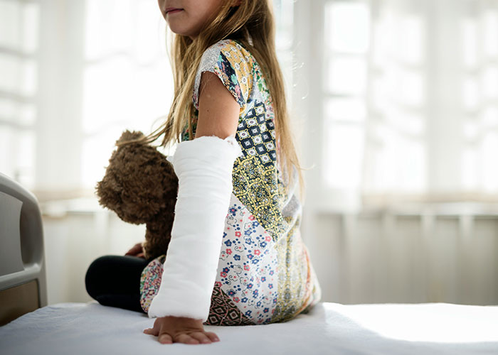 Young girl with a cast on her arm sitting on a bed, holding a teddy bear, highlighting unsettling medical facts.