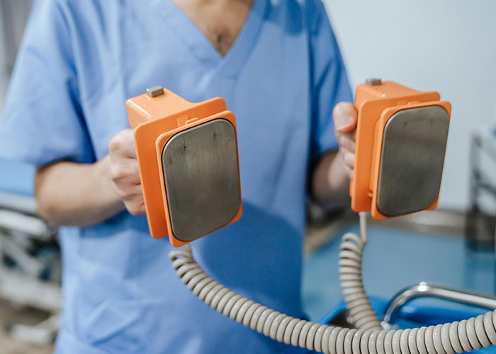 Medical professional in scrubs holding defibrillator paddles, highlighting unsettling medical equipment.