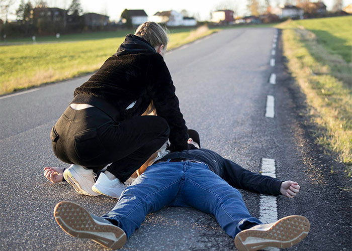 Person kneeling to assist another lying on the road, illustrating unsettling medical emergency situation.