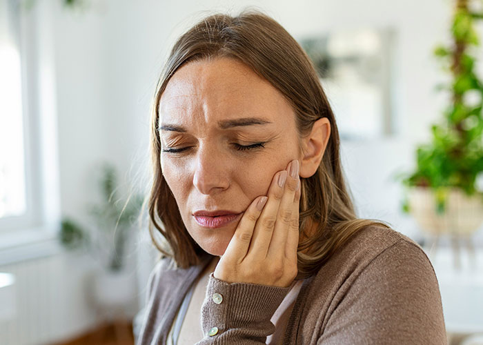 Woman in discomfort holding her cheek, possibly experiencing an unsettling medical issue.