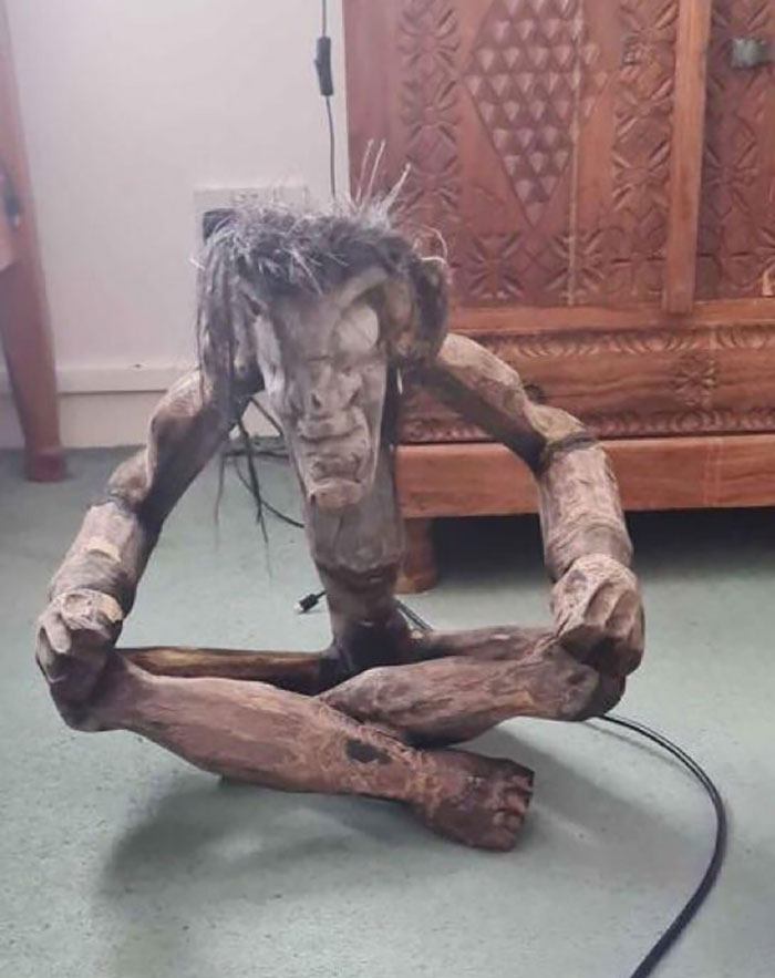 A creepy wooden sculpture with a haunting expression sits on the floor, suitable for selling online.