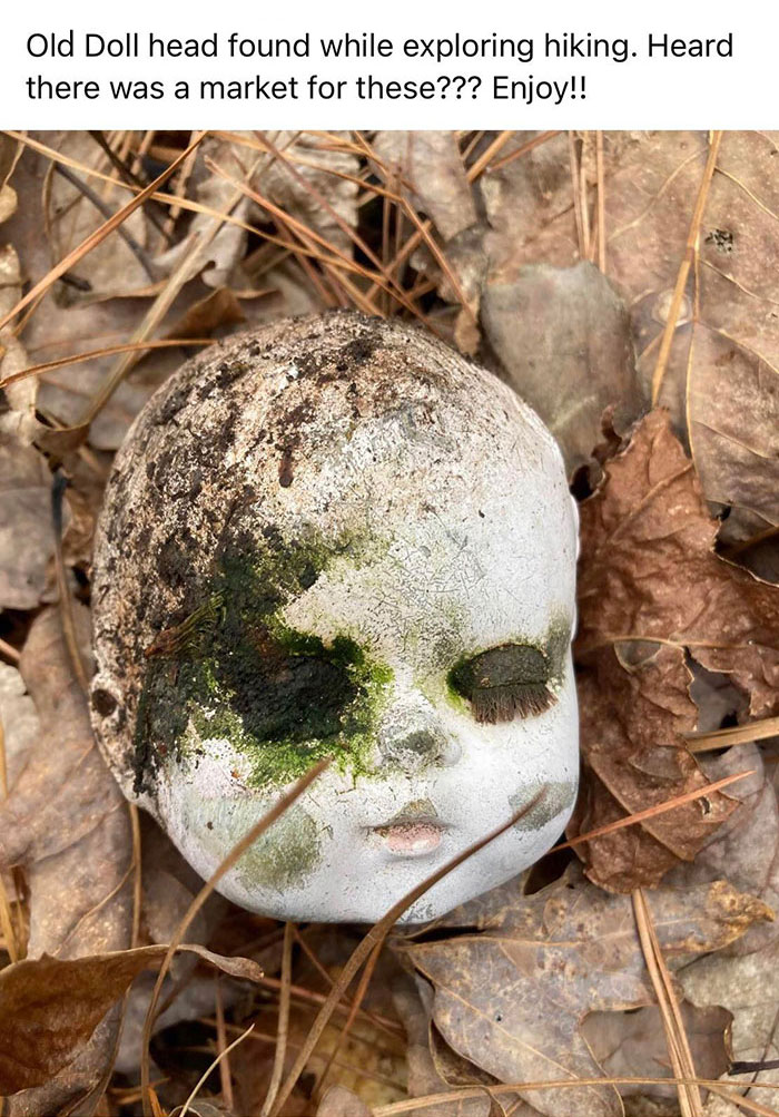 Creepy old doll head covered in moss and dirt on a bed of autumn leaves.