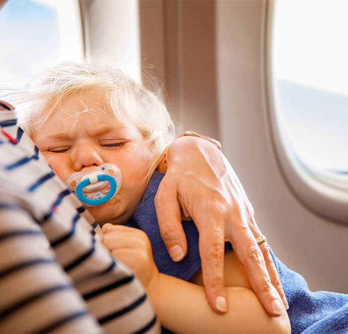 Crying child with pacifier being comforted on airplane, related to seat swap incident.