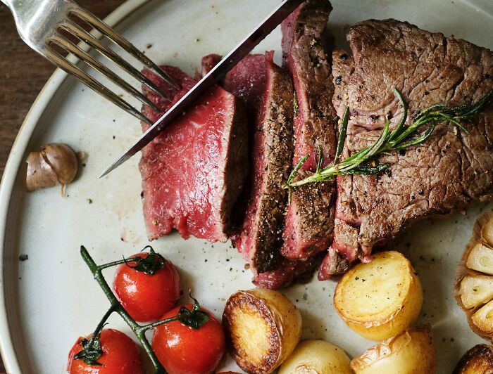 Sliced steak with rosemary, cherry tomatoes, and potatoes on a plate, showcasing expensive items worth spending money.