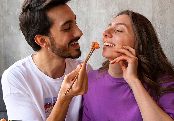 Partners sharing a playful moment while eating sushi, highlighting adorable relationship dynamics.